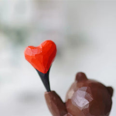 A closer view of the bear figure with a heart balloon shows the hand-carved details.