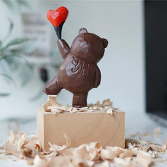 Front view of wood sculpture bear with heart balloon placed on a block of wood showcasing the hand carved features.