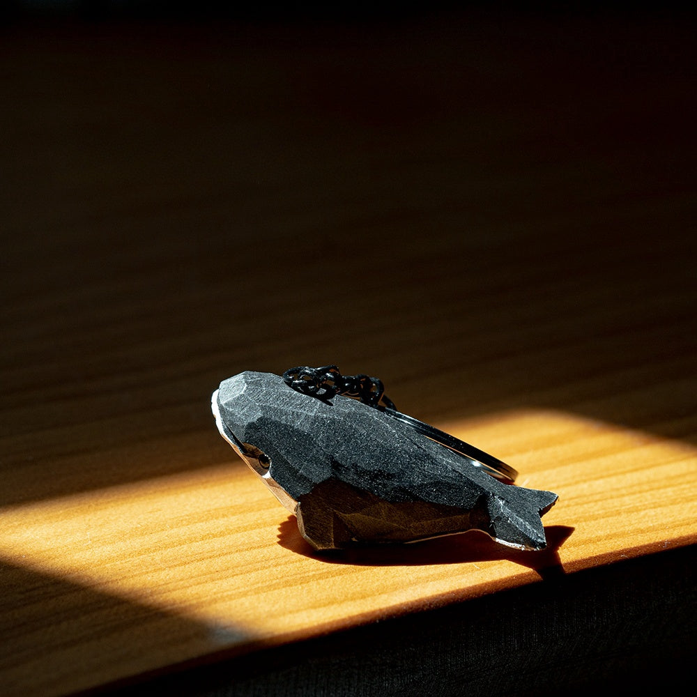 Black whale keychain lying on a wooden surface, emphasizing its design in sunlight.