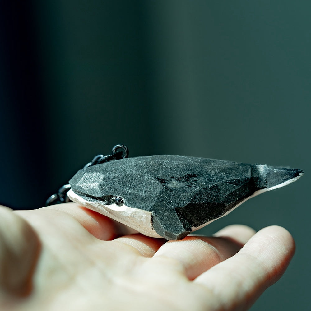 Hand holding a black whale keychain, capturing its intricate carvings.