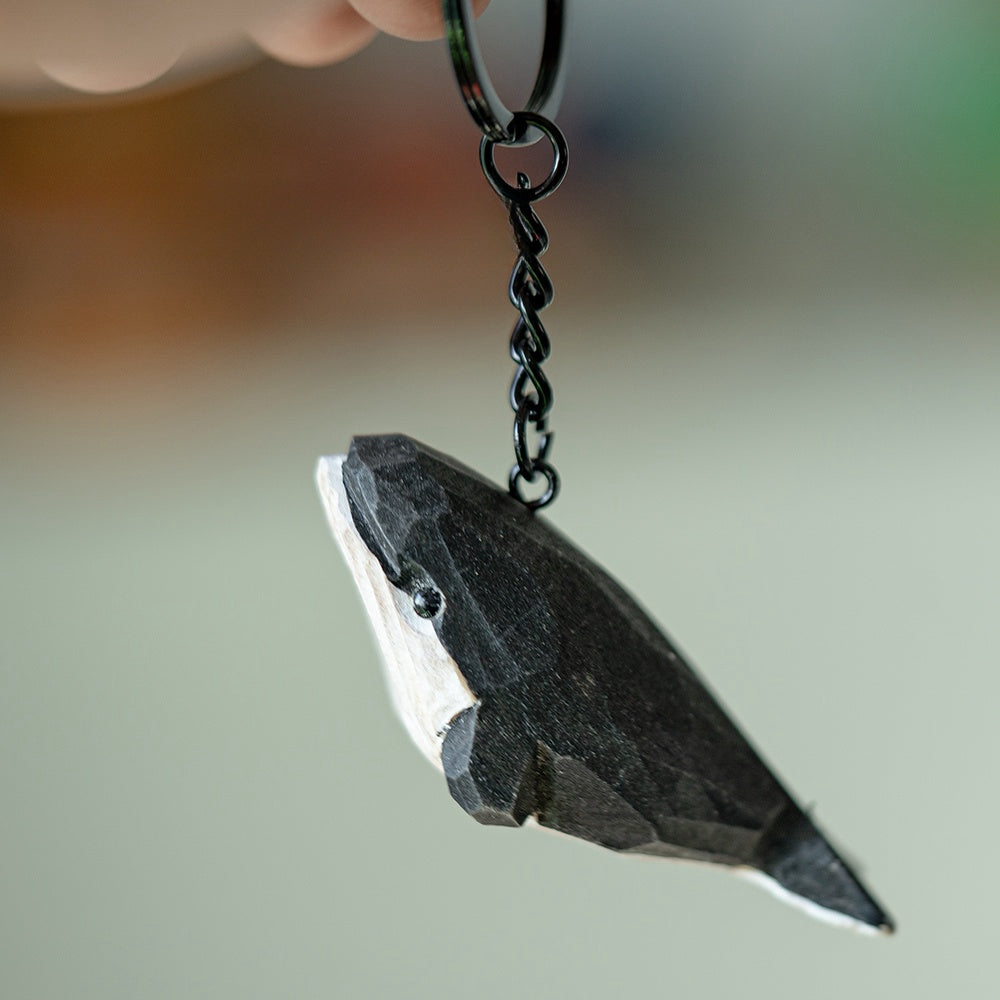 Hand-carved black whale keychain hanging, showing its detailed engraving.