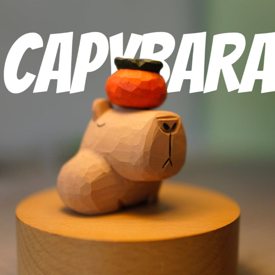 The capybara figurine is placed on a wooden platform with a small persimmon on its head.