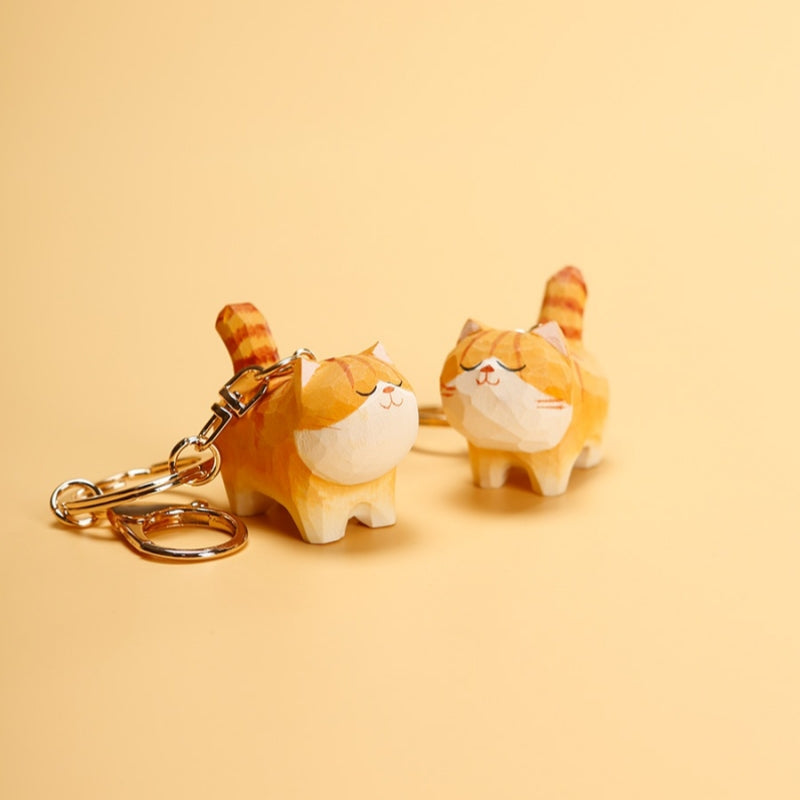 Hand-carved Chubby Orange Cat Keychain with gold ring on beige background