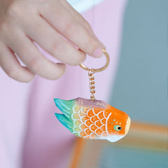 Close-up of a hand holding a colorful fish keychain with bright orange and green scales, highlighting the detailed design.