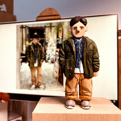 Custom figurine of a young man in a green jacket and tan pants, hand-carved from wood.