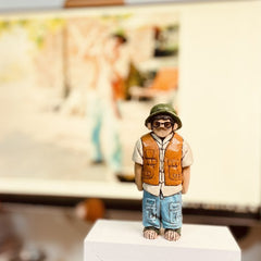 Custom figurine of a young man in a brown vest and blue pants, wearing glasses and a hat, hand-carved from wood.