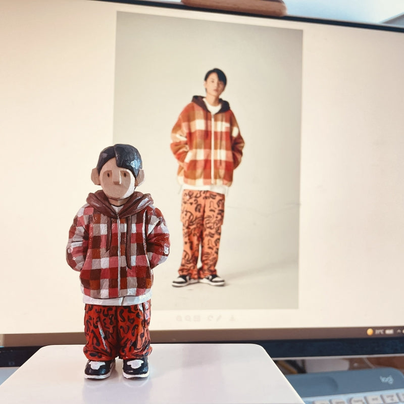 Custom figurine of a young man in a red checkered hoodie and patterned pants, hand-carved from wood.