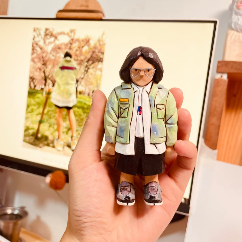 Custom figurine of a young woman in a green jacket and glasses, hand-carved from wood.