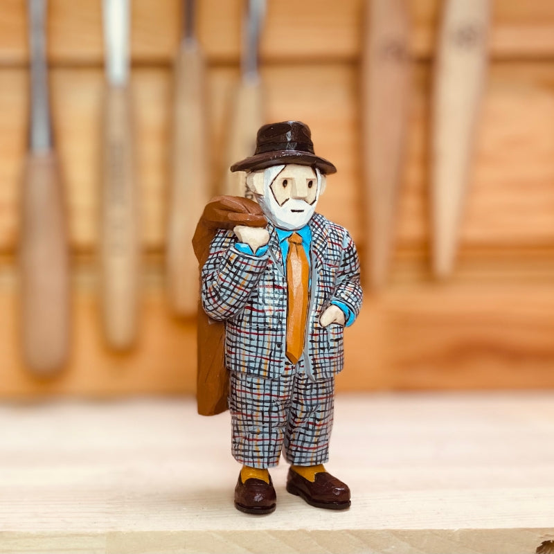 Custom figurine of an elderly man in a checkered suit and hat, carrying a bag, hand-carved from wood.