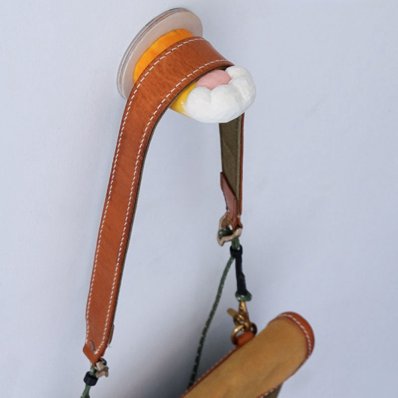 Handcrafted wooden cat’s claw handle used as a hook for hanging a leather strap on a white wall.