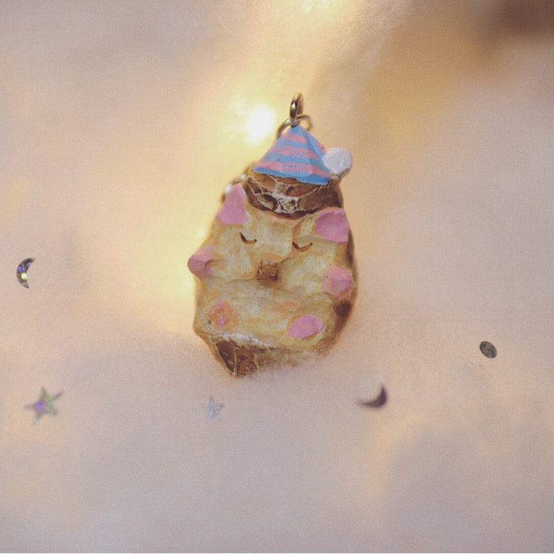 Hedgehog keychain with pastel-painted details and a tiny party hat, placed on a soft, illuminated surface.