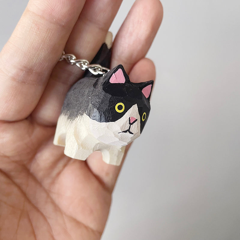 Hand-painted Holstein cat keychain with big yellow eyes, held in a hand to show scale and craftsmanship.