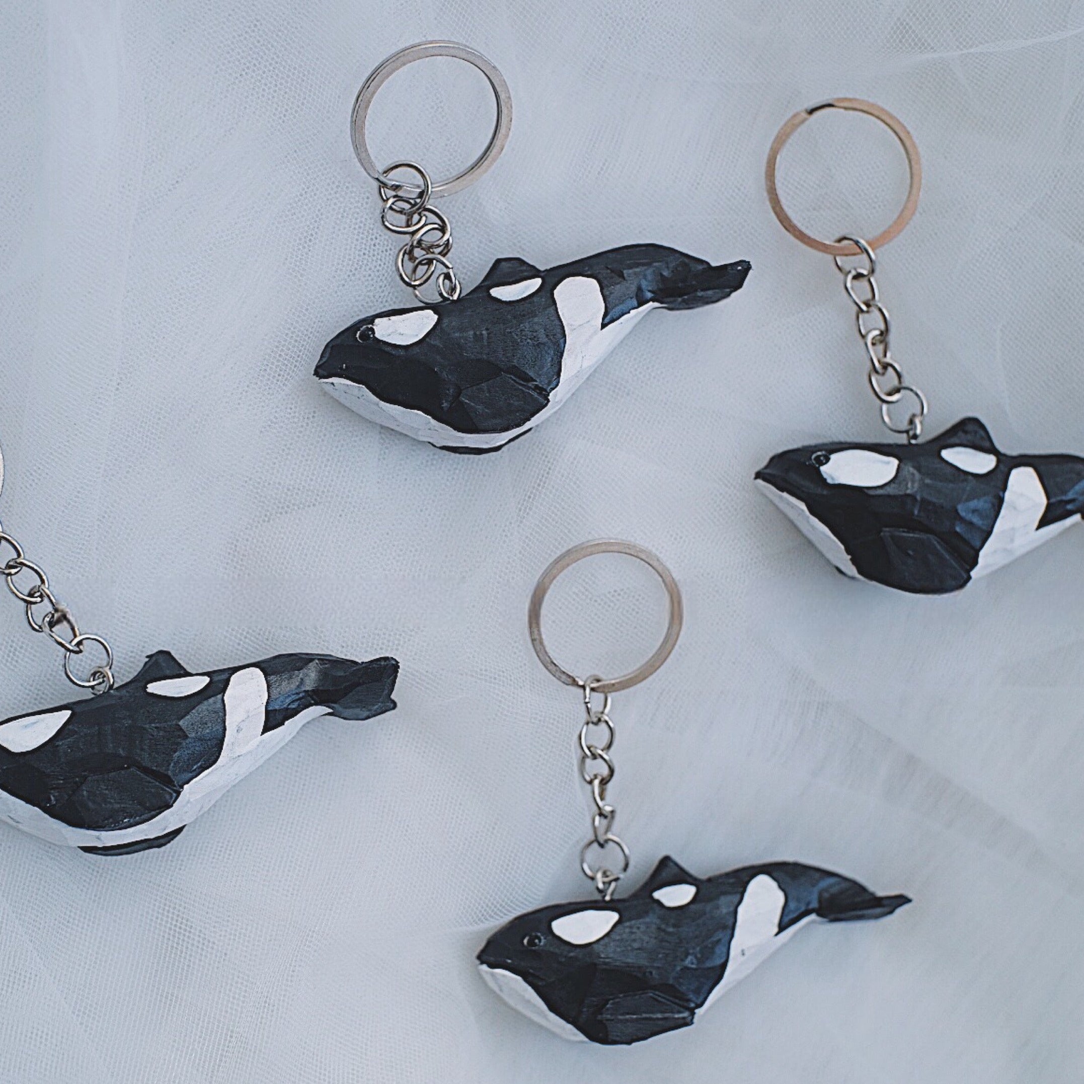 Four hand-carved orca whale keychains arranged on a white fabric background.