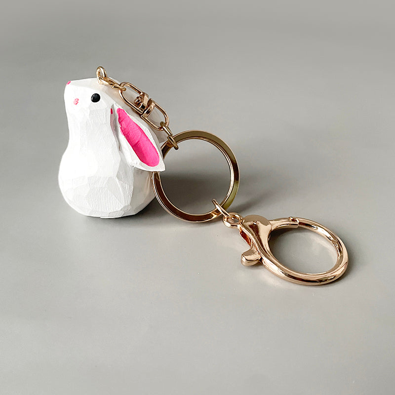 Side view of a handmade bunny keychain, showcasing its white body and pink ears, with a golden keyring.