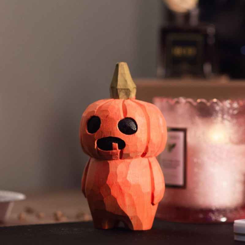 Orange hand-carved pumpkin head wooden figurine on display.