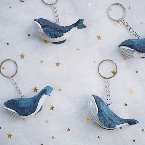 Four swimming whale keychains displayed on a starry fabric, showing different angles.