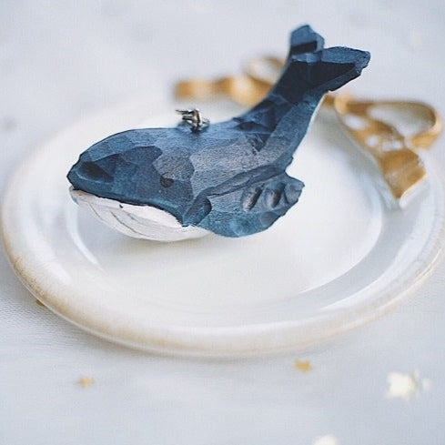 Hand-carved swimming whale keychain resting on a decorative plate with starry background.